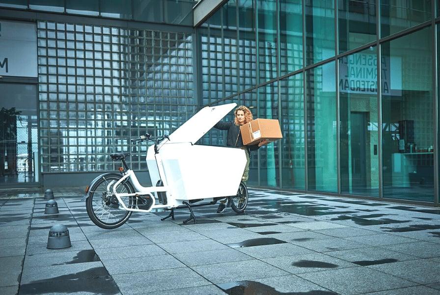 Frau mit Lastenrad transportiert Karton vor modernem Gebäude