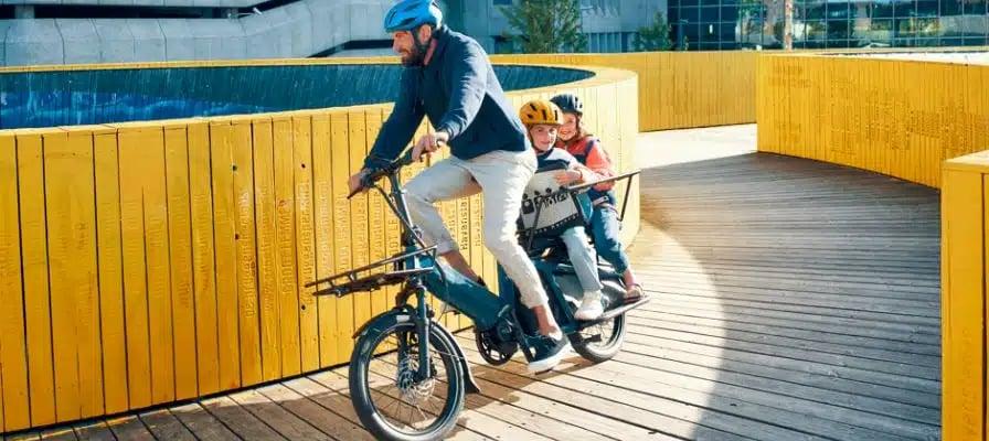 Vater mit Kindern auf einem E-Bike unterwegs auf Holzweg