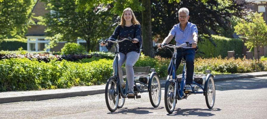 Zwei Personen fahren auf Dreirädern auf einer sonnigen Straße