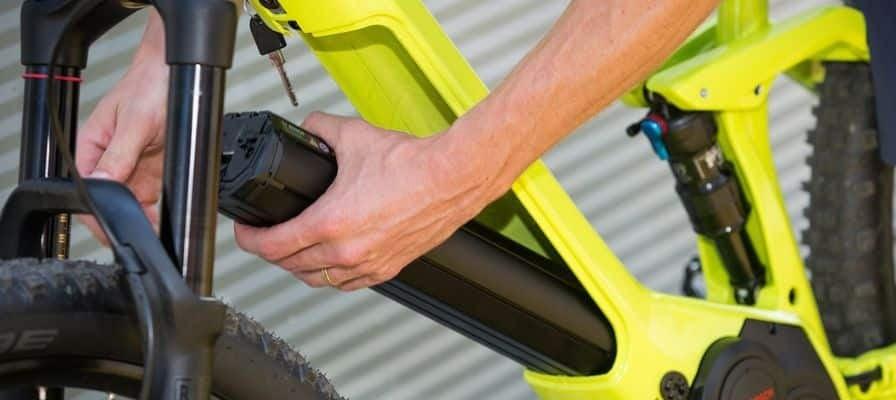 Person entfernt Akku von gelbem E-Bike vor Wellblechwand