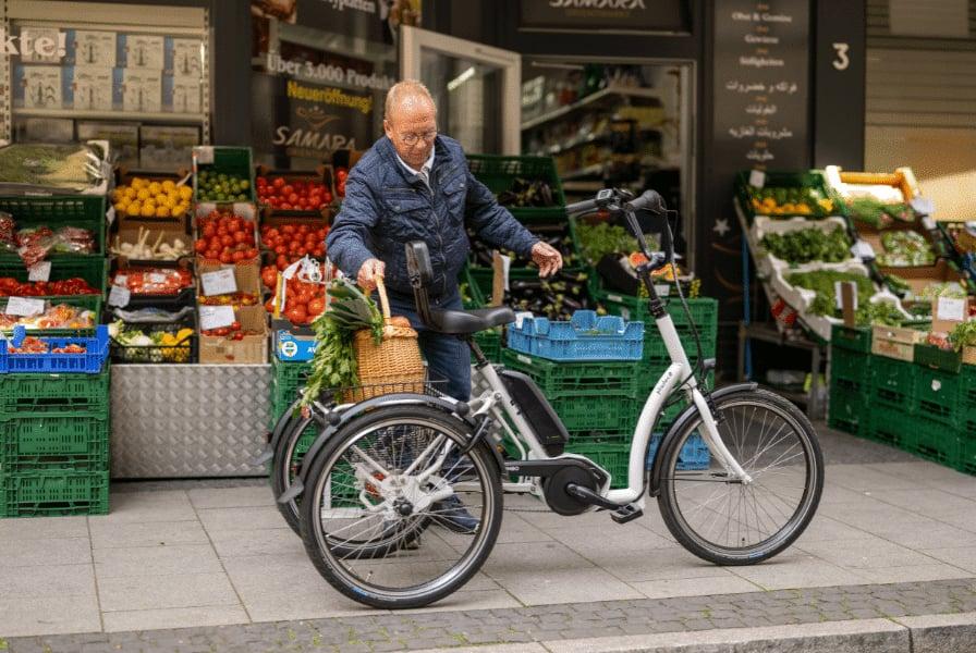 Mann mit E-Bike vor einem Obst- und GemĂĽseladen