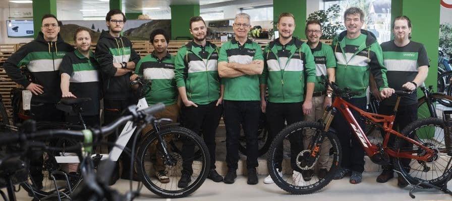 Teamfoto in Fahrradgeschäft mit E-Bikes und Mitarbeitern in grüner Kleidung
