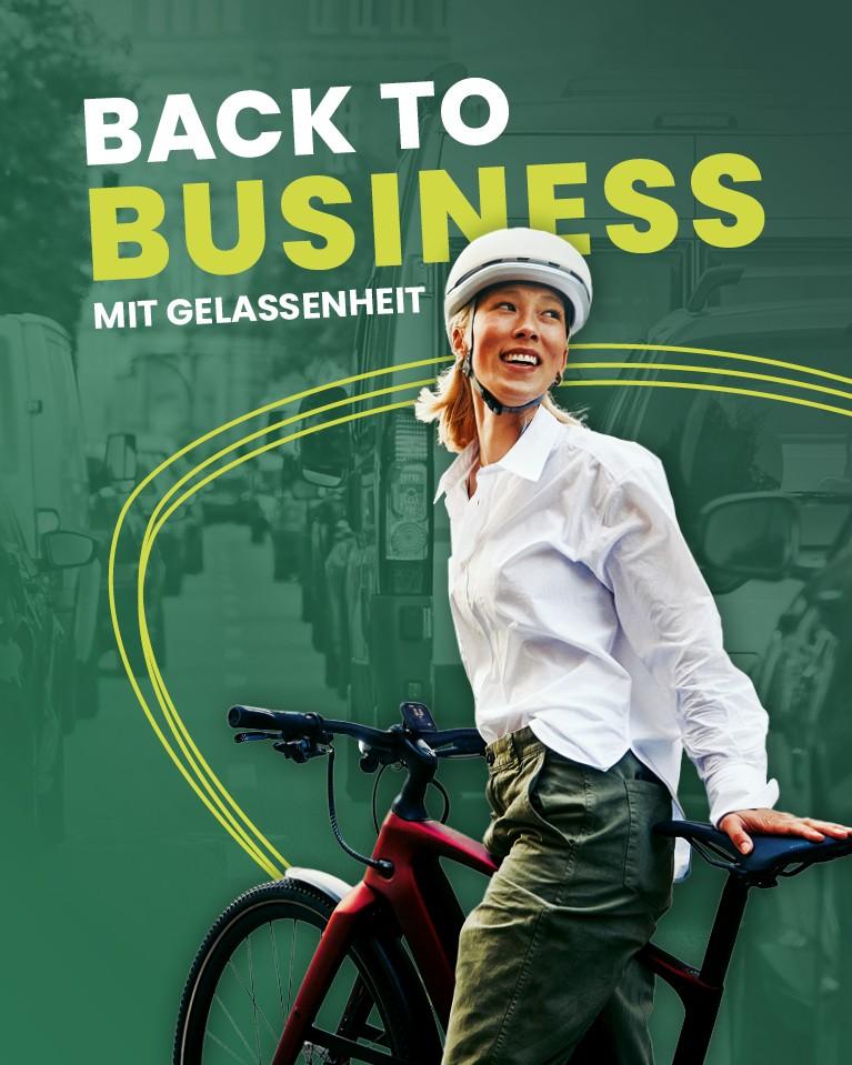 Eine Frau mit Helm steht mit ihrem City e-Bike vor einer befahrenen Straße
