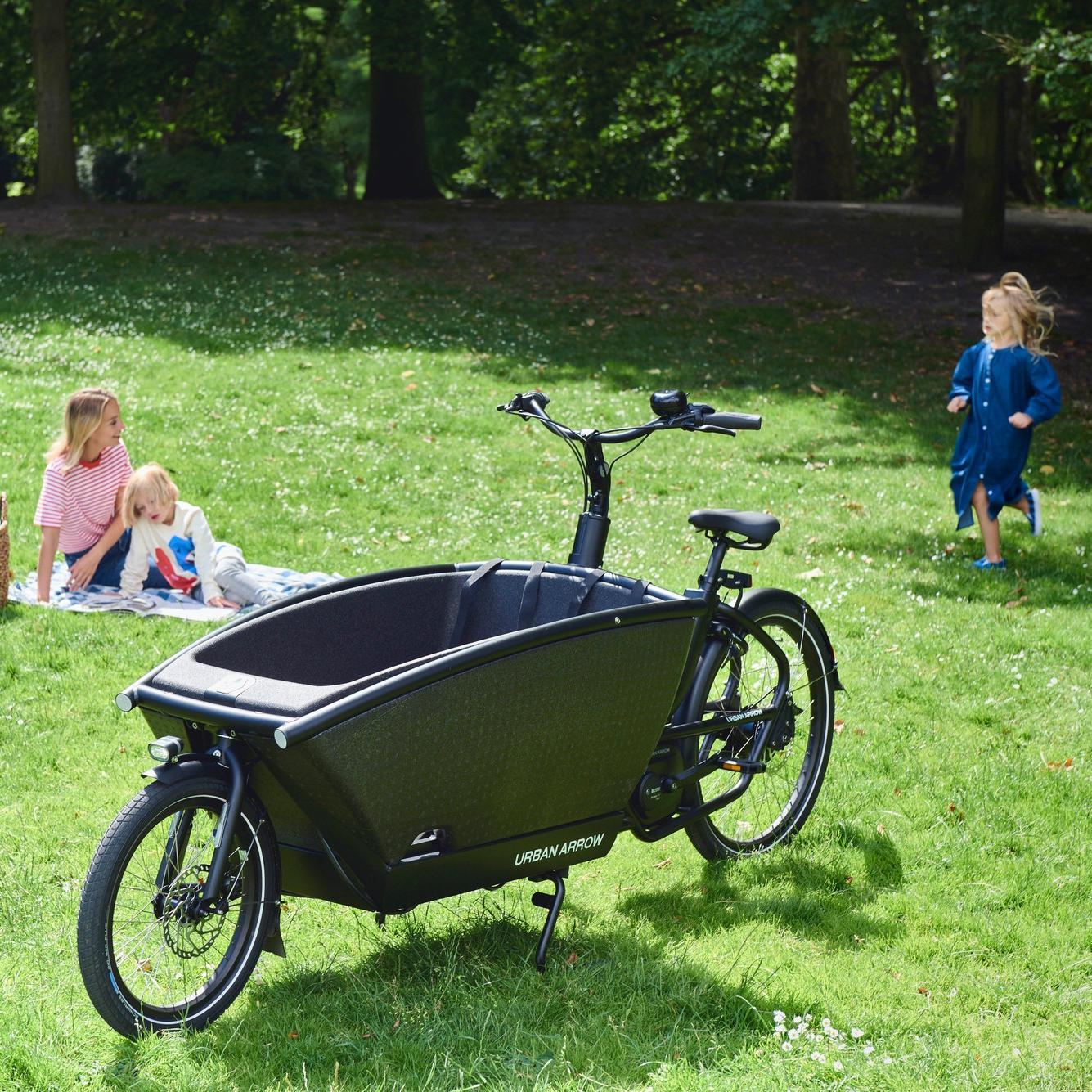 Urban Arrow Family auf der Wiese, auf einer Decke im Hintergrund Frau und Kinder