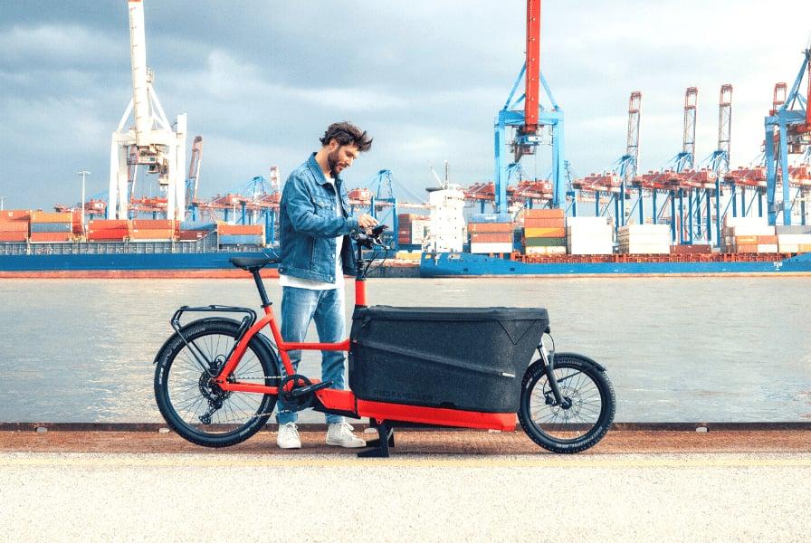 Mann mit Lastenrad vor Hafenkränen und Containern