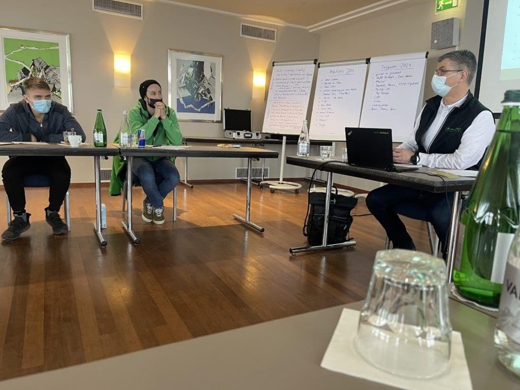 Besprechung in Konferenzraum mit drei Personen und Präsentation