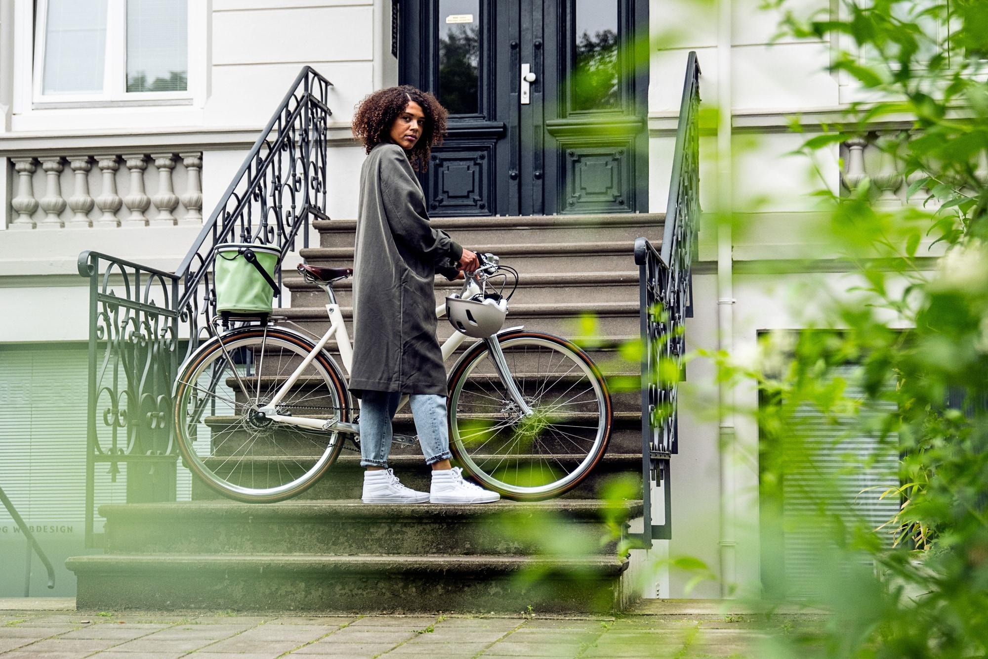 Eine Person mit einem modernen Stadtrad steht vor einer eleganten Haustür. Ideal für urbane Mobilität mit Stil.