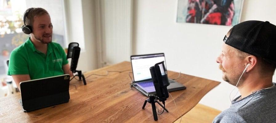 Zwei Männer im Gespräch mit Mikrofonen und Laptops bei einem Podcast