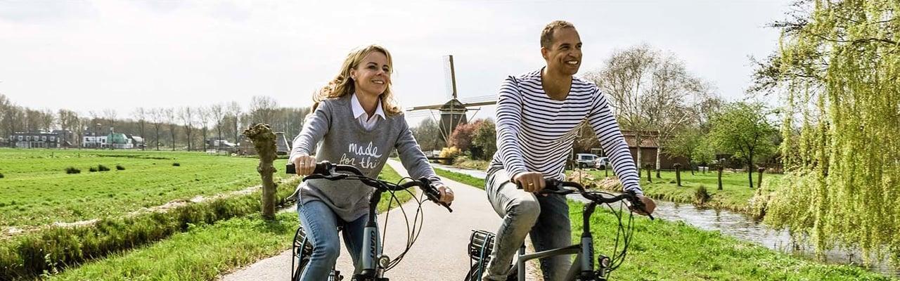 Zwei Personen fahren Fahrräder auf ländlicher Straße mit Windmühle im Hintergrund