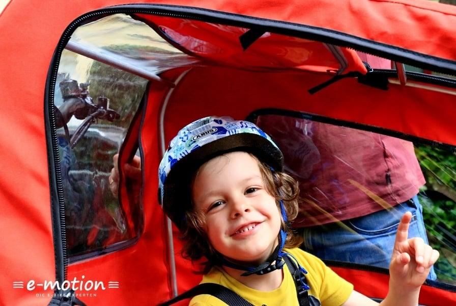 Kind mit Helm in rotem Fahrradanhänger von e-motion