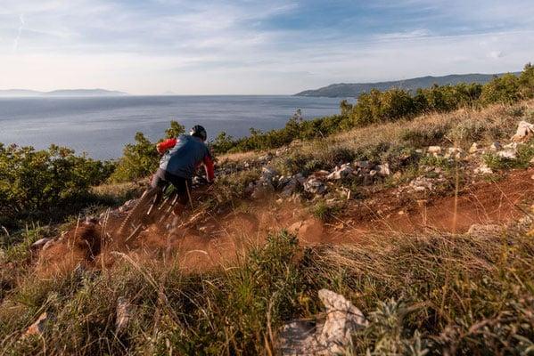 Mountainbiker auf steinigem Pfad mit Meerblick bei Sonnenuntergang