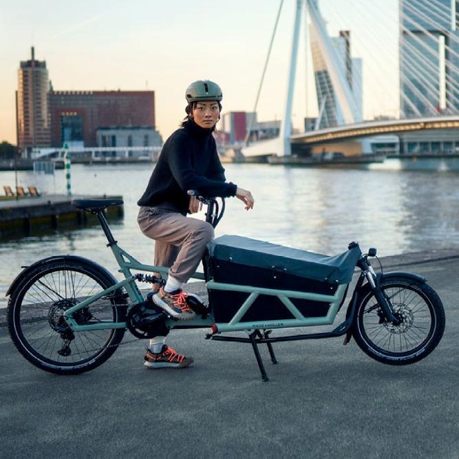 Eine Frau sitzt auf ihrem Riese & Müller Load4 60 Cargo e-Bike und steht vor dem Wasser