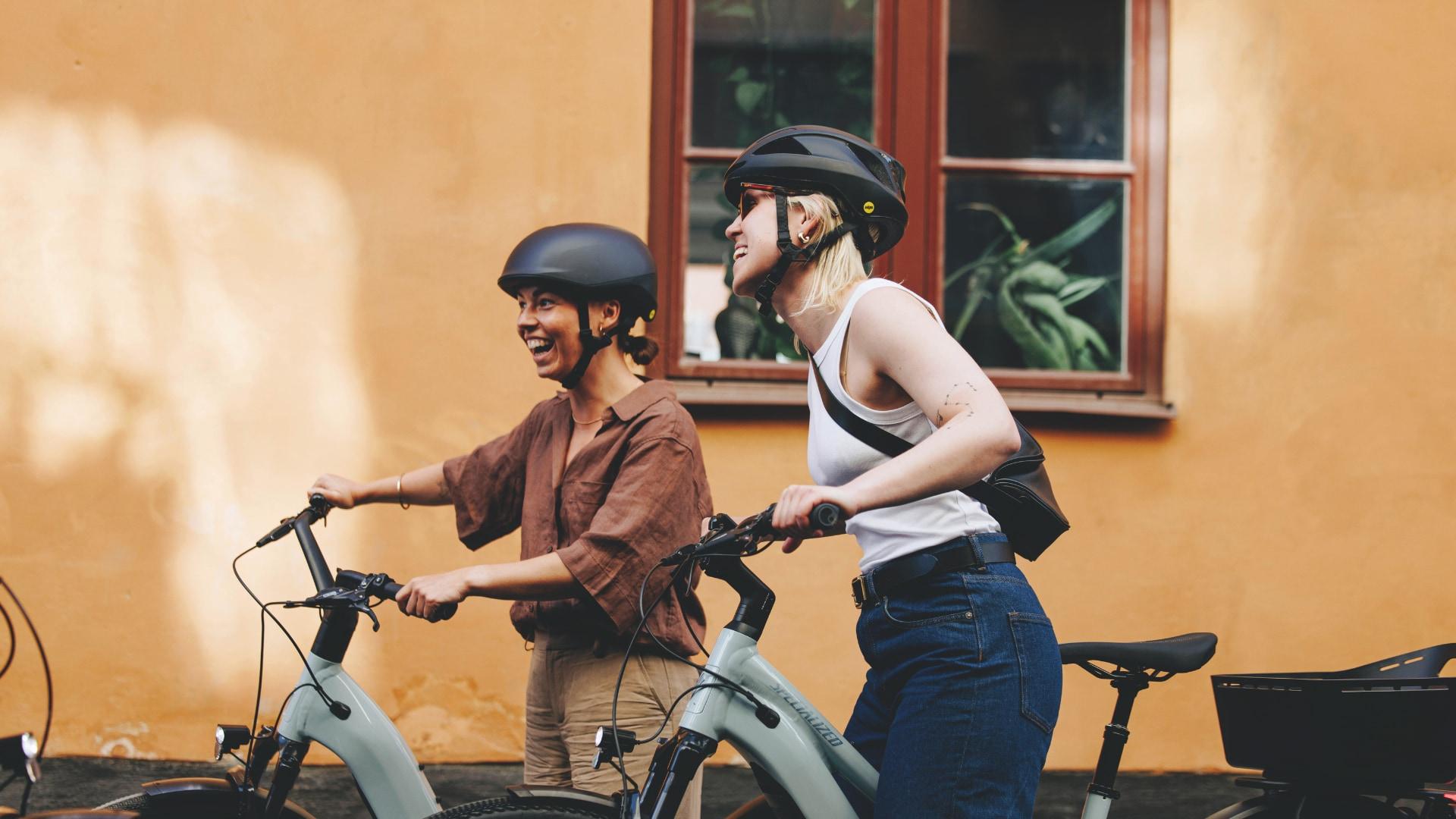 Zwei e-Bike Fahrerinnen schieben das Specialized Como Rad durch die Stadt