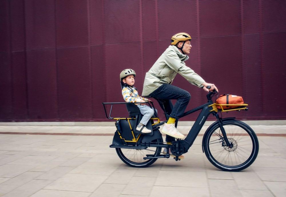 Mann und Kind auf Riese & Müller Lastenrad vor roter Wand