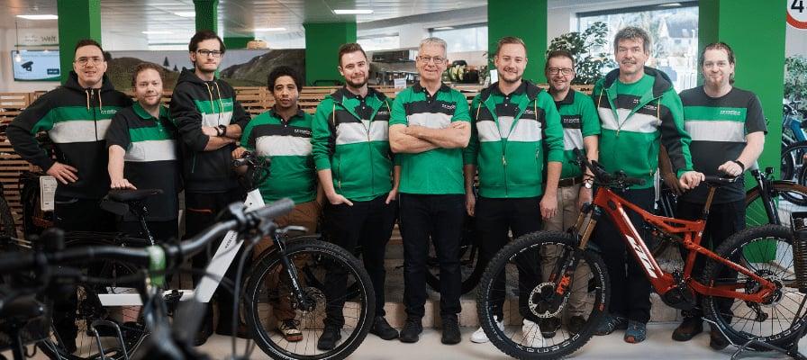 Team in grüner Arbeitskleidung in einem Fahrradgeschäft mit E-Bikes