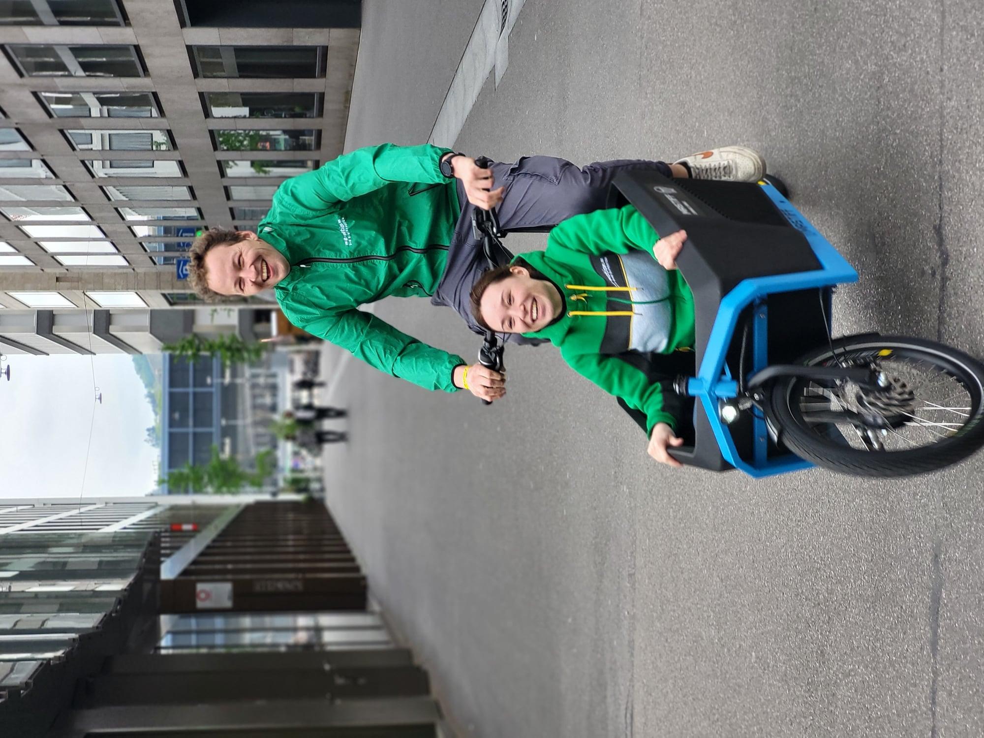 Zwei Personen fahren auf einem Lastenrad durch die Stadt