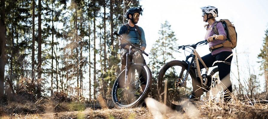 Zwei Personen mit Mountainbikes im Wald bei sonnigem Wetter