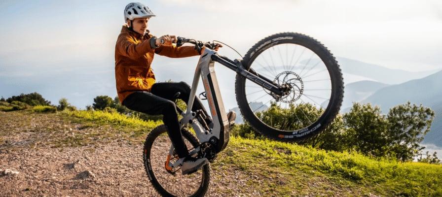 Mann macht Wheelie auf Simplon Rapcon PMAX PINION E-Bike in bergiger Landschaft
