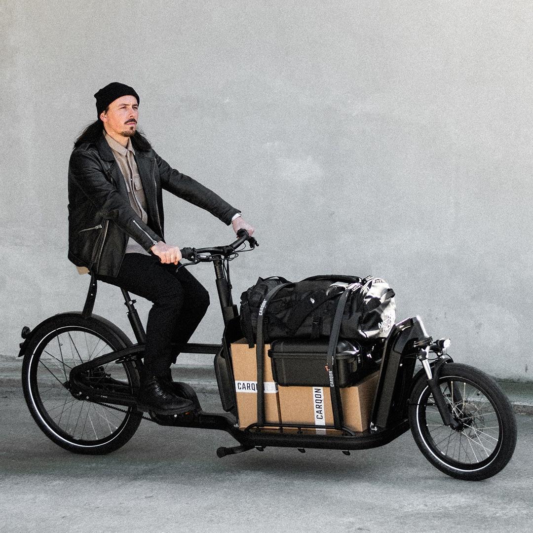 Ein Mann fährt mit dem Lasten e-Bike Carqon Flatbed und Ladung die Straße entlang