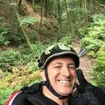 Mann mit Helm im Wald, lächelnd mit Daumen hoch