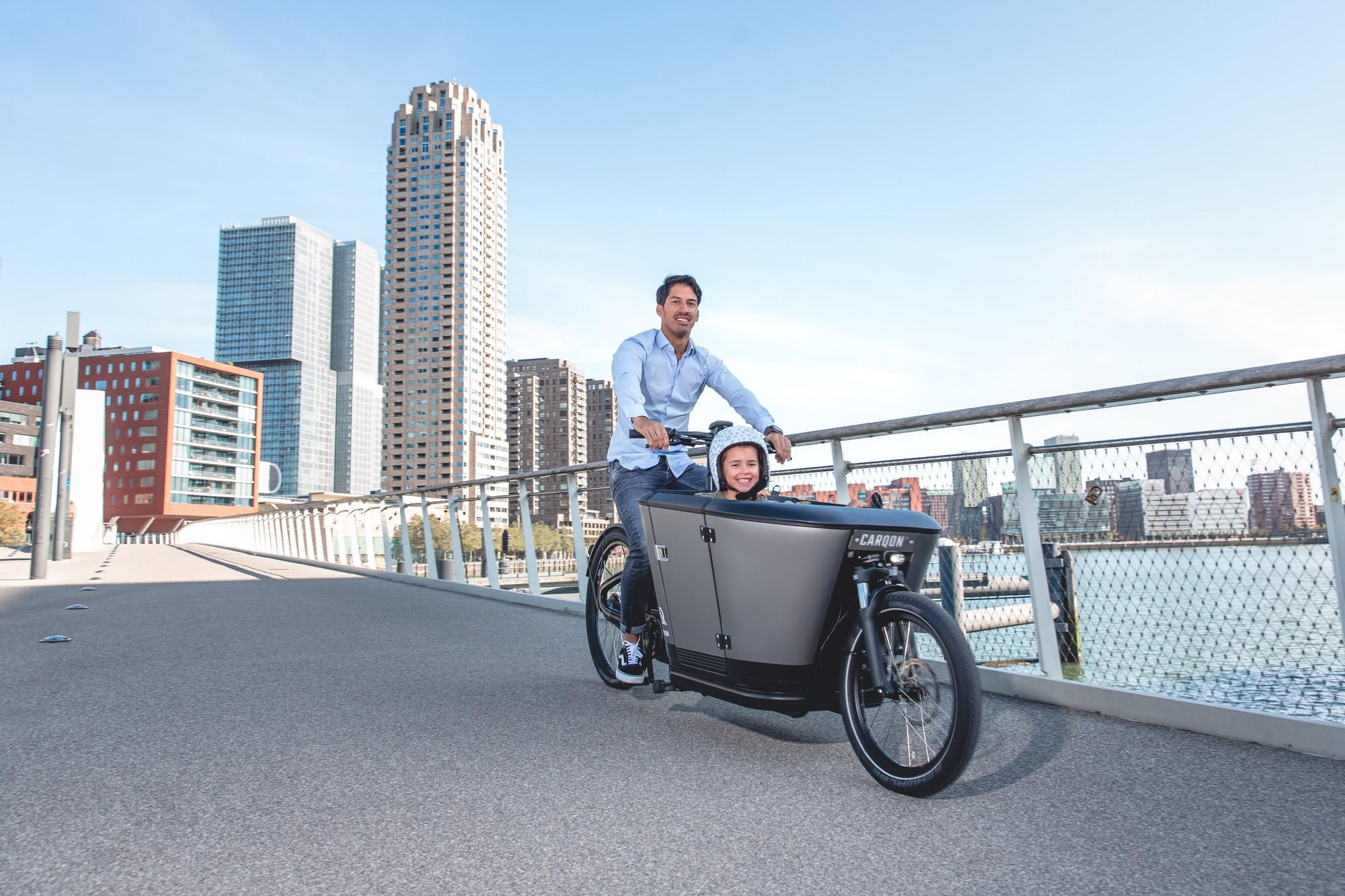 Das Bild zeigt ein Carqon E-Lastenrad, das von einem Mann  in einer städtischen Umgebung gefahren wird.