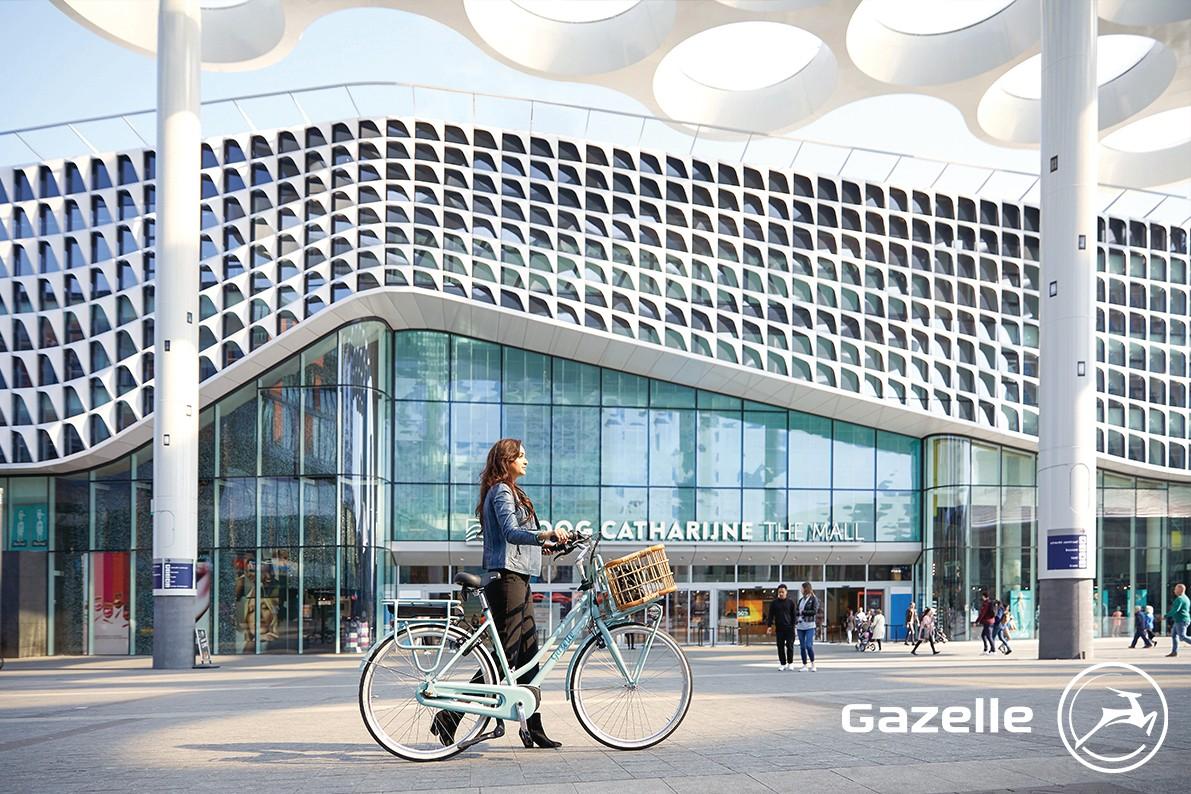 Eine Frau schiebt das Gazelle e-Bike Miss Grace vor einem Bahnhof entlang