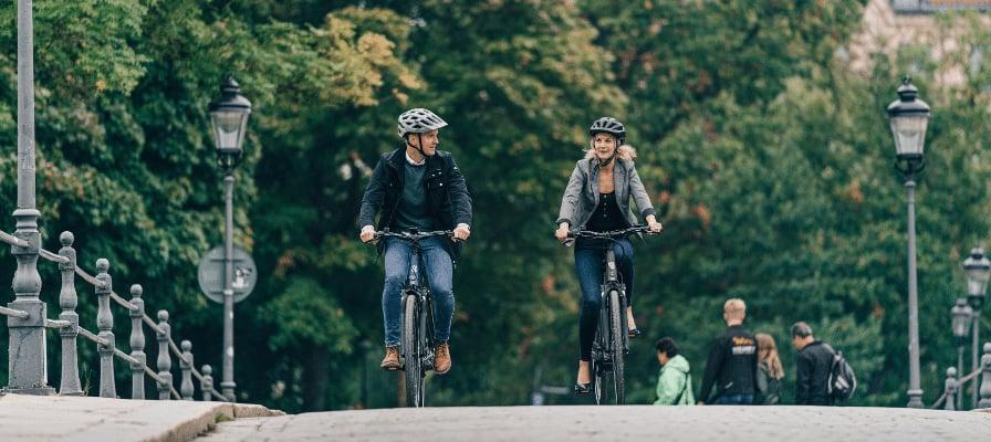 Zwei Personen fahren auf E-Bikes über eine Brücke in einer grünen Umgebung