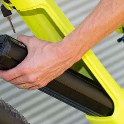 Person entfernt Akku von gelbem E-Bike vor Wellblechwand
