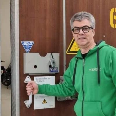 Mann in grüner Jacke öffnet große Holztür mit Schild