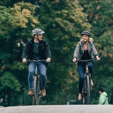 Zwei Personen fahren auf E-Bikes über eine Brücke in einer grünen Umgebung