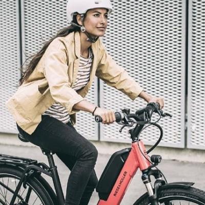 Frau auf E-Bike mit rotem Rahmen fährt vor Metallzaun