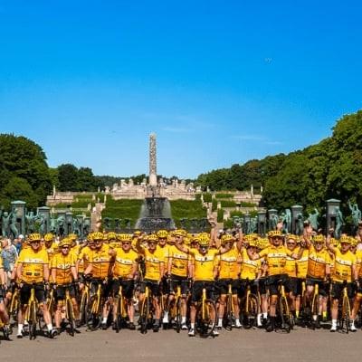 Gruppe von Radfahrern in gelben Trikots vor monumentalem Park