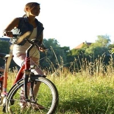 Frau mit E-Bike in sonniger Landschaft vor historischer Kulisse