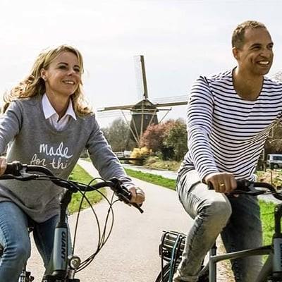 Zwei Personen fahren Fahrräder auf ländlicher Straße mit Windmühle im Hintergrund