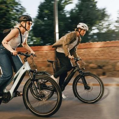 Zwei Personen fahren E-Bikes auf einer Straße bei Sonnenuntergang