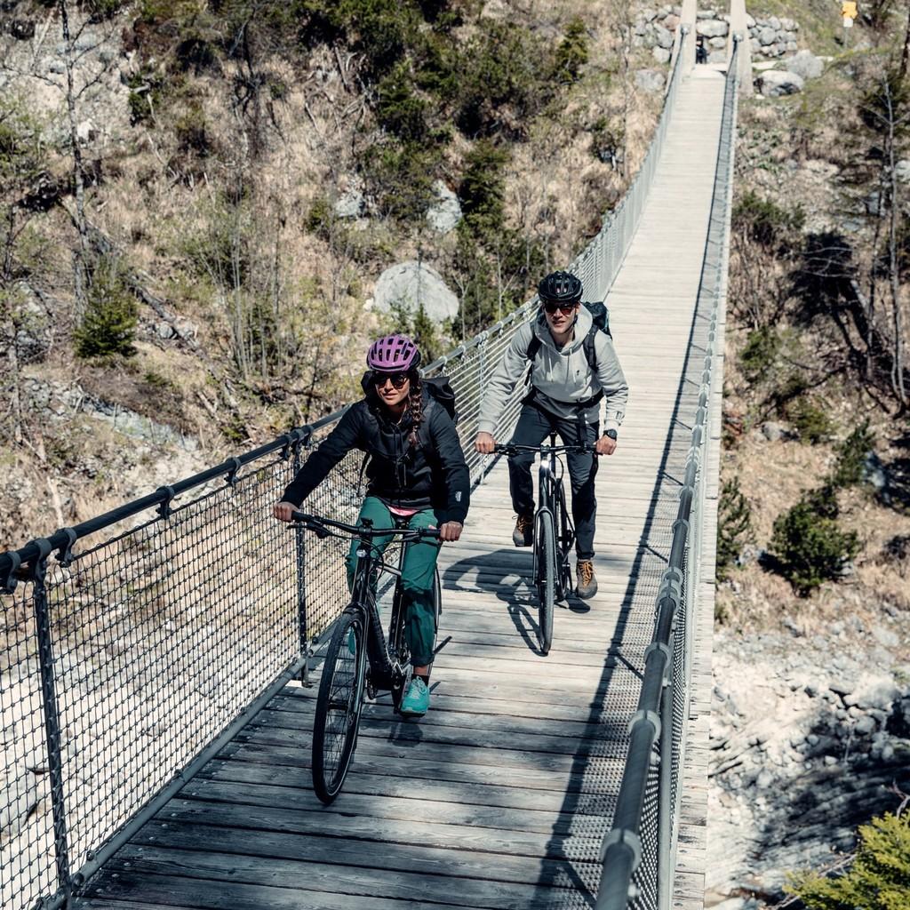 Zwei Radfahrer überqueren eine beeindruckende Hängebrücke inmitten einer malerischen Naturlandschaft. Ideal für abe