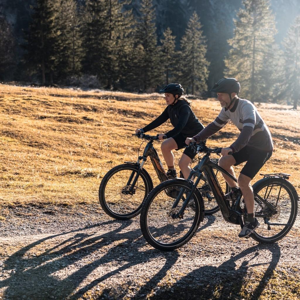 Zwei junge Menschen fahren auf einem Trekking e-Bike durch die herbstliche Landschaft.