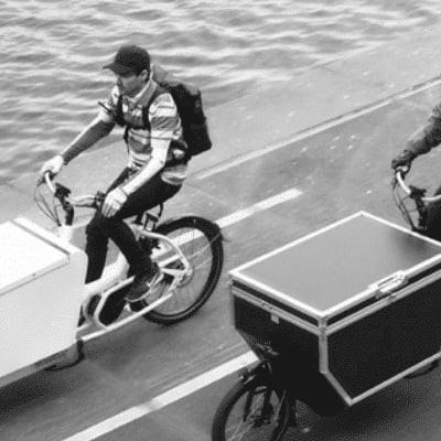 Zwei Lasten-e-Bikes mit großen Transportboxen am Flussufer