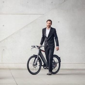 Mann im Anzug mit Stromer ST2 S E-Bike vor moderner Betonwand