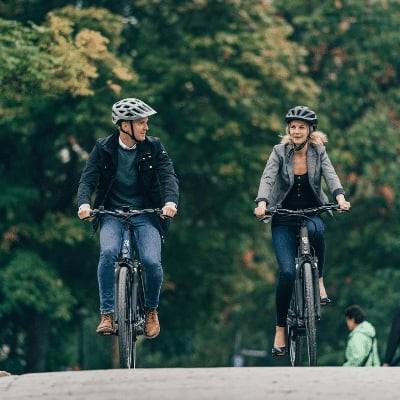 Zwei Personen fahren auf E-Bikes über eine Brücke in einer grünen Umgebung
