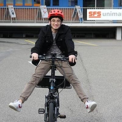 Mann auf E-Bike vor Pestalozzi-Gebäude mit rotem Helm