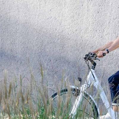 Frau auf E-Bike fährt vor grauer Wand mit Gras im Vordergrund