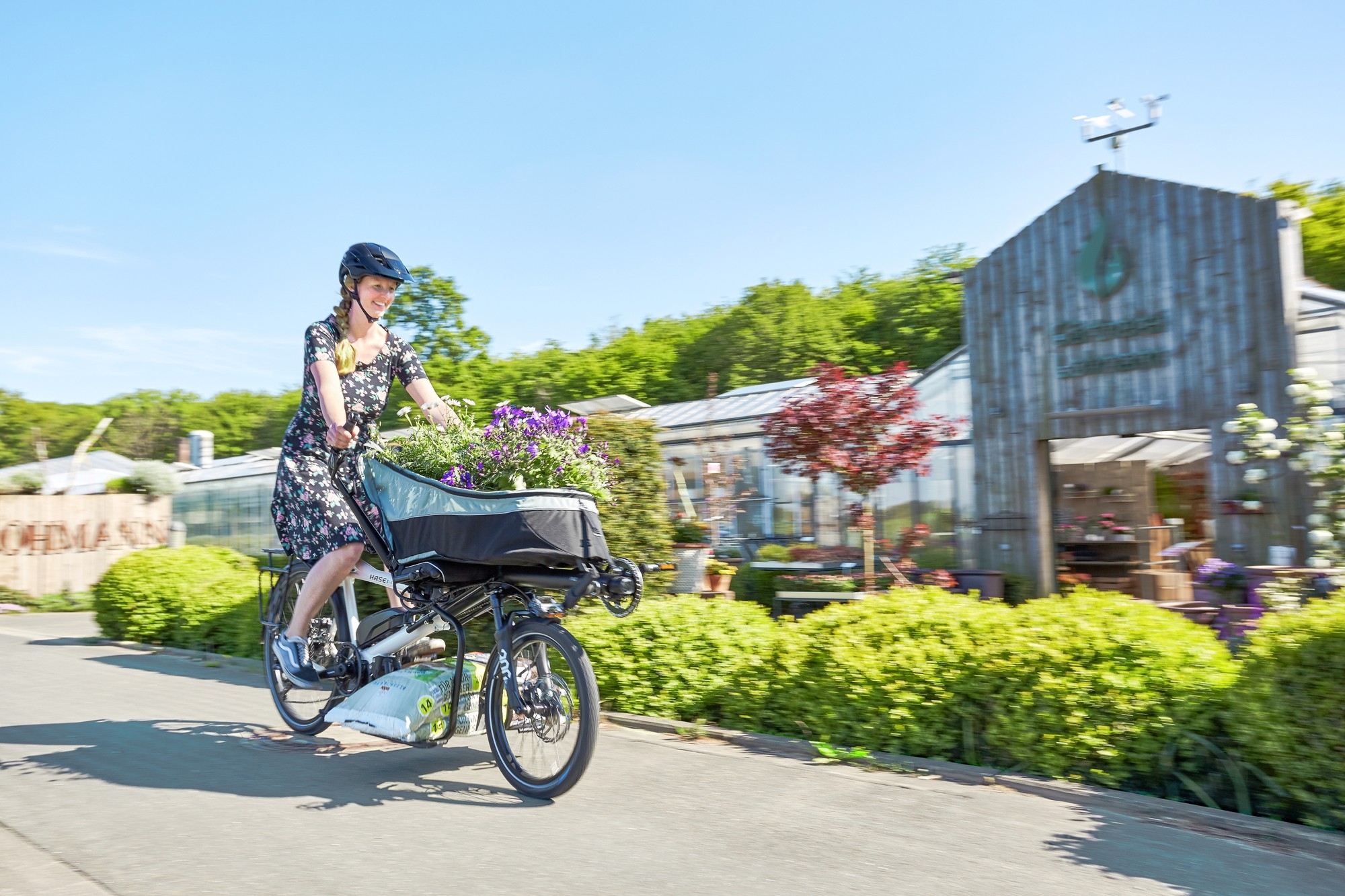 Das Bild zeigt eine Frau auf einem Hase Bikes e-Dreirad, die Blumen transportiert