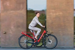 Pendlerin auf rotem E-Bike fährt vor moderner Architektur