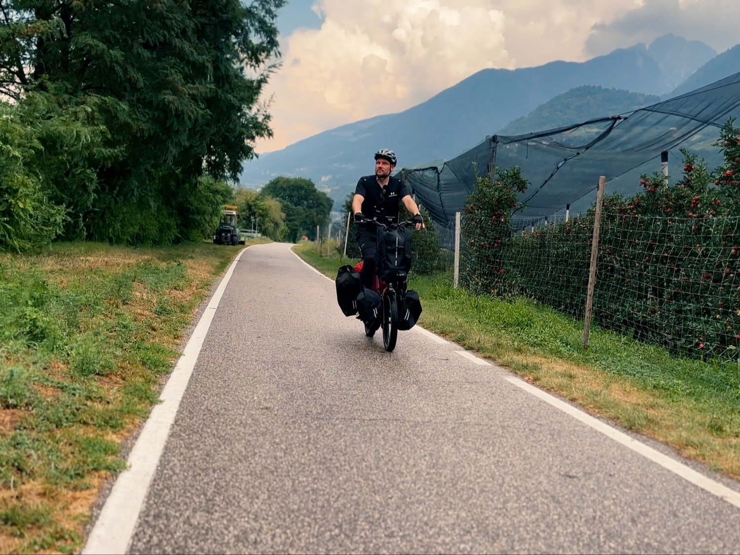 Das Bild zeigt einen E-Bike-Fahrer, der auf einem schmalen Weg entlang einer Apfelplantage fährt.