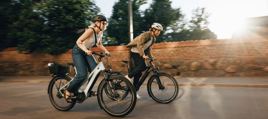 Zwei Personen fahren E-Bikes auf einer Straße bei Sonnenuntergang