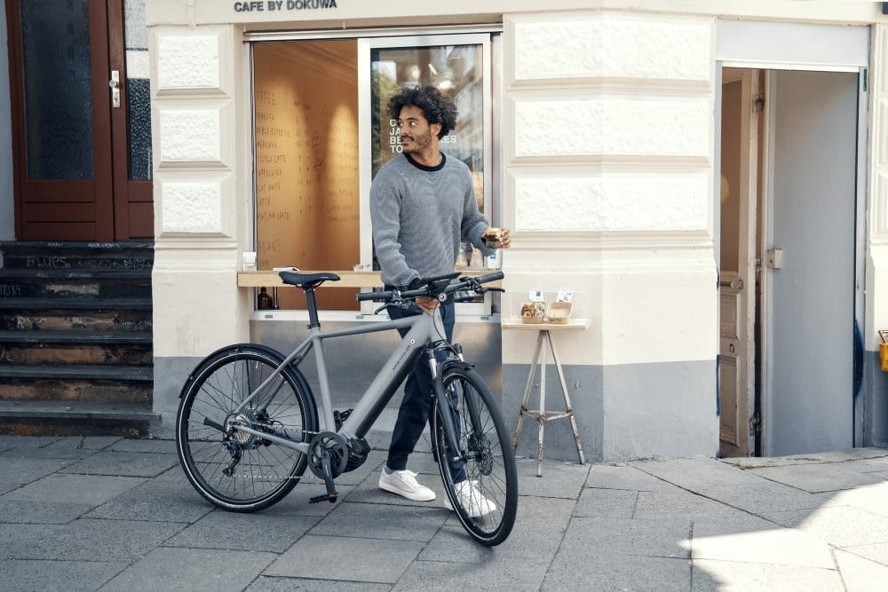 Mann mit grauem E-Bike vor einem Café