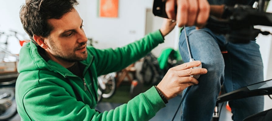 Fahrradmontage: Mann in grüner Jacke justiert Sattel