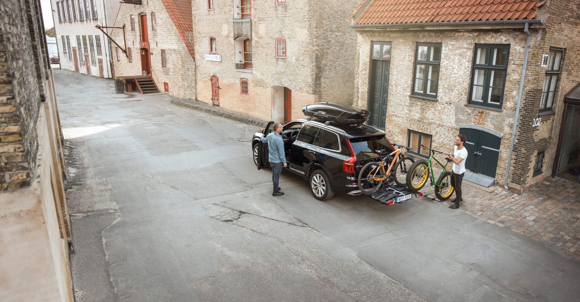 Zwei Personen stehen neben einem Auto mit Thule-Anhänger und zwei e-Bikes