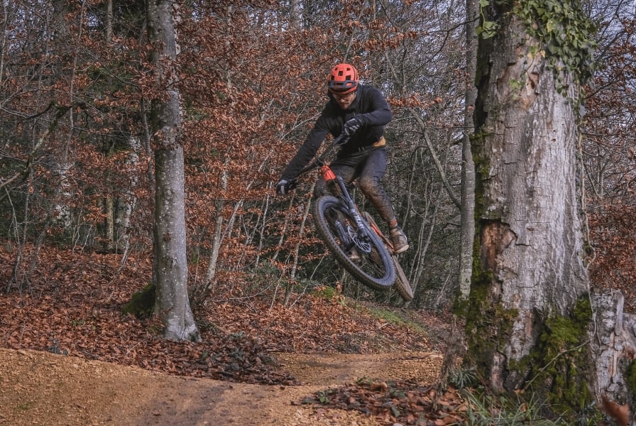 Mountainbiker springt durch herbstlichen Wald auf kurviger Strecke